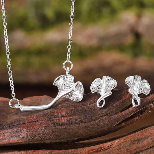 Silver ginkgo leaf necklace and earrings on a wooden surface with a natural background