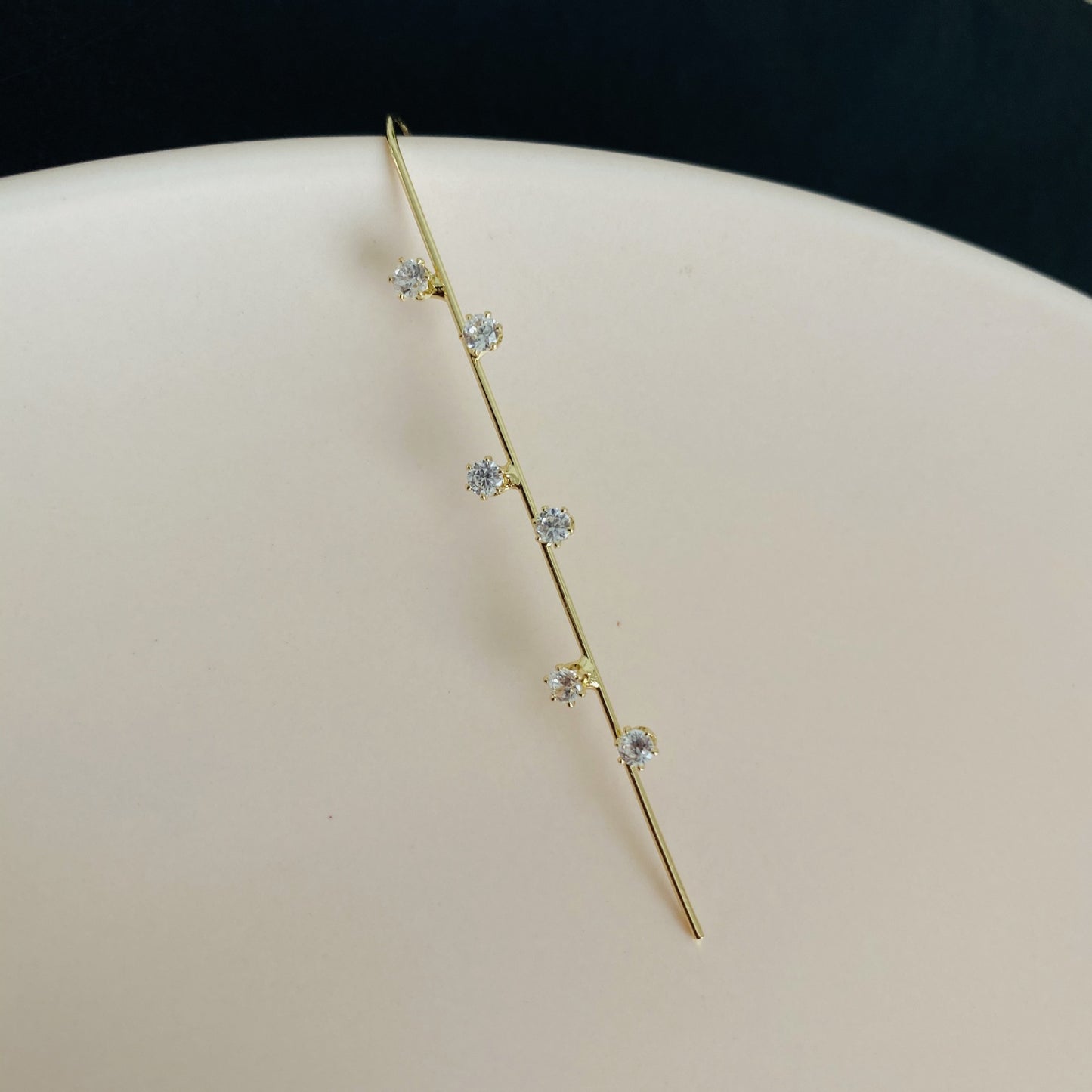 Gold ear cuff with diamond-like stones on a white surface