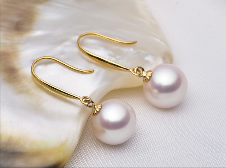 Pearl earrings with gold hooks on a shell background