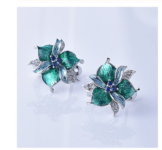Pair of green floral earrings with blue gemstones on a light gray background