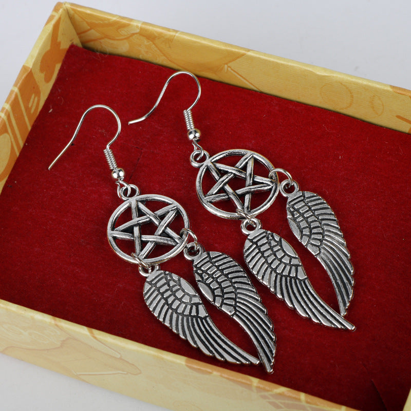 Silver winged pentacle earrings on a red and wooden surface