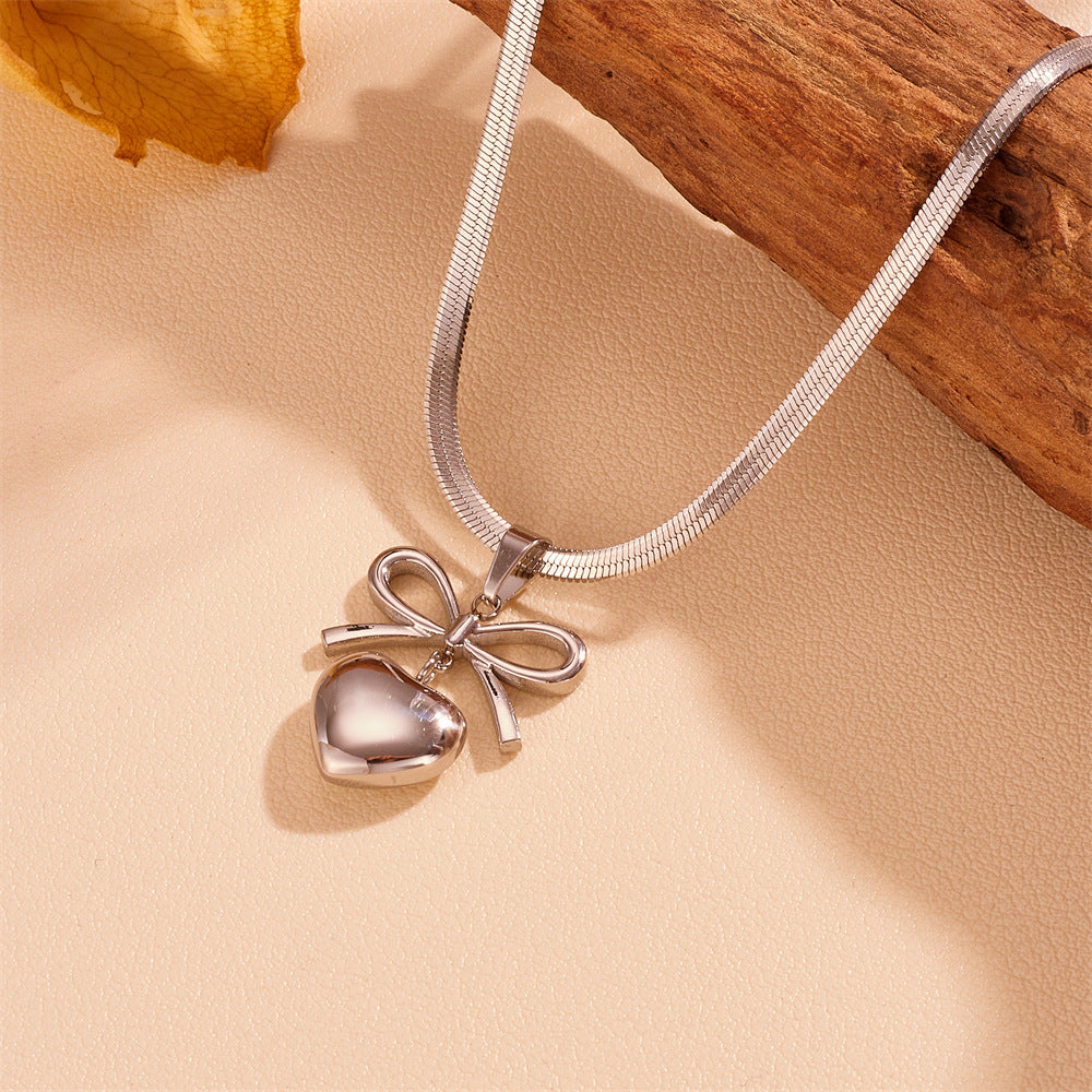 Silver necklace with a heart and bow pendant on a beige surface.