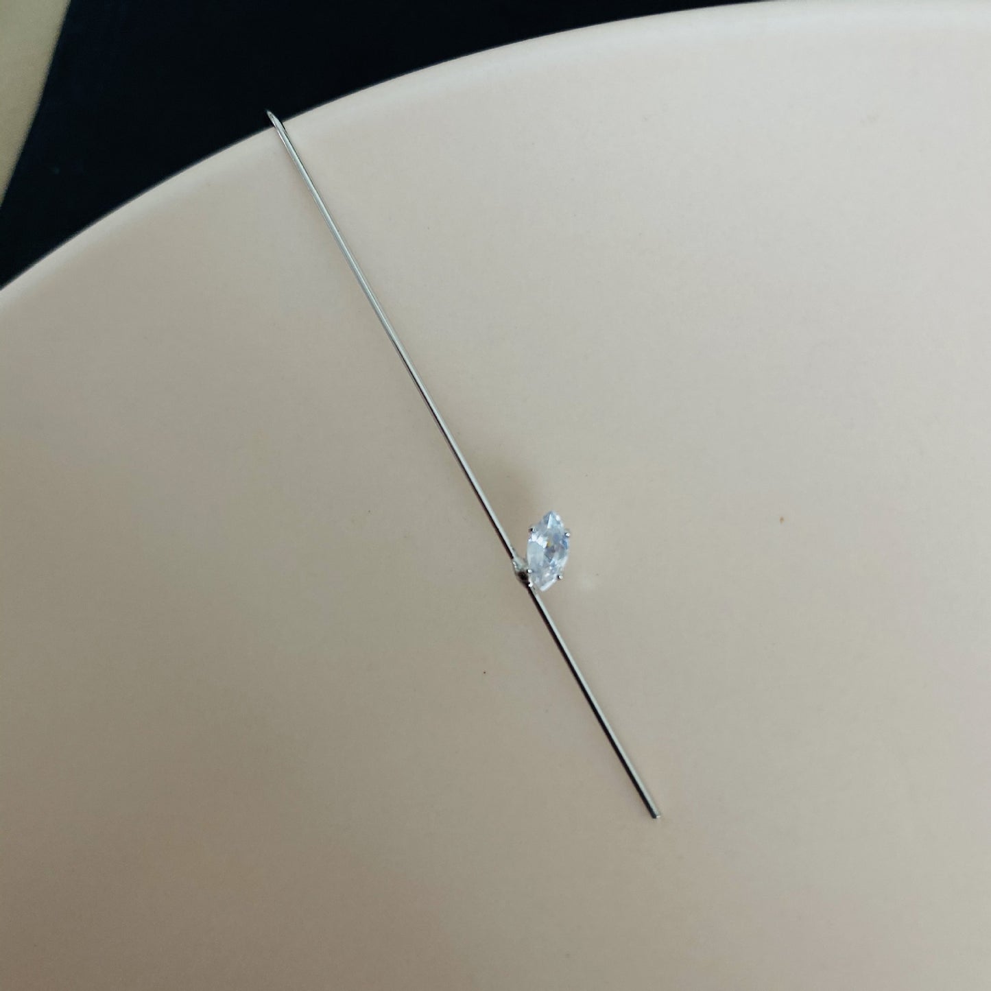 Small diamond on a thin metal rod against a beige background
