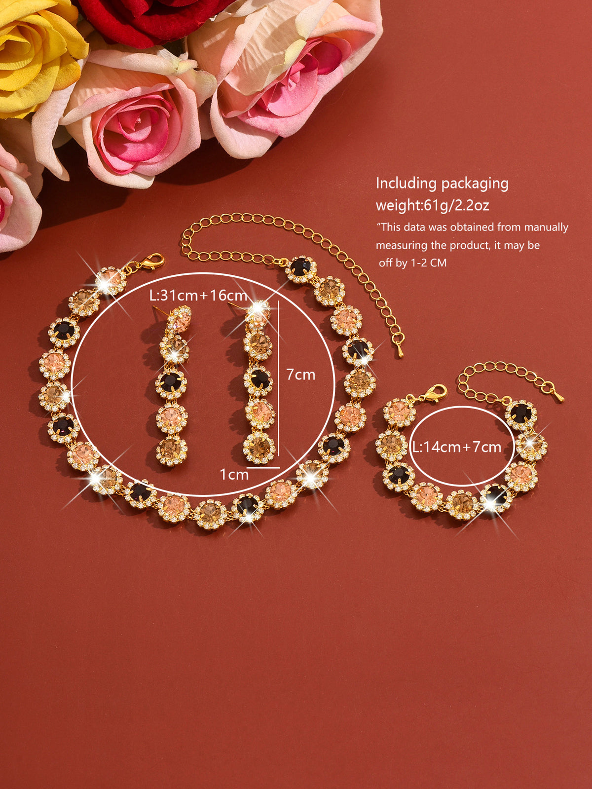 Gold-tone jewelry set with floral rhinestone details, shown on a warm red-brown background with flowers in the top left and printed measurement callouts and weight text.