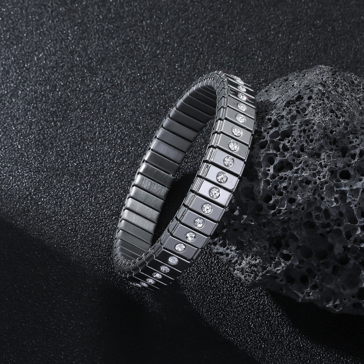 Black metal bracelet with embedded diamonds on a textured black surface