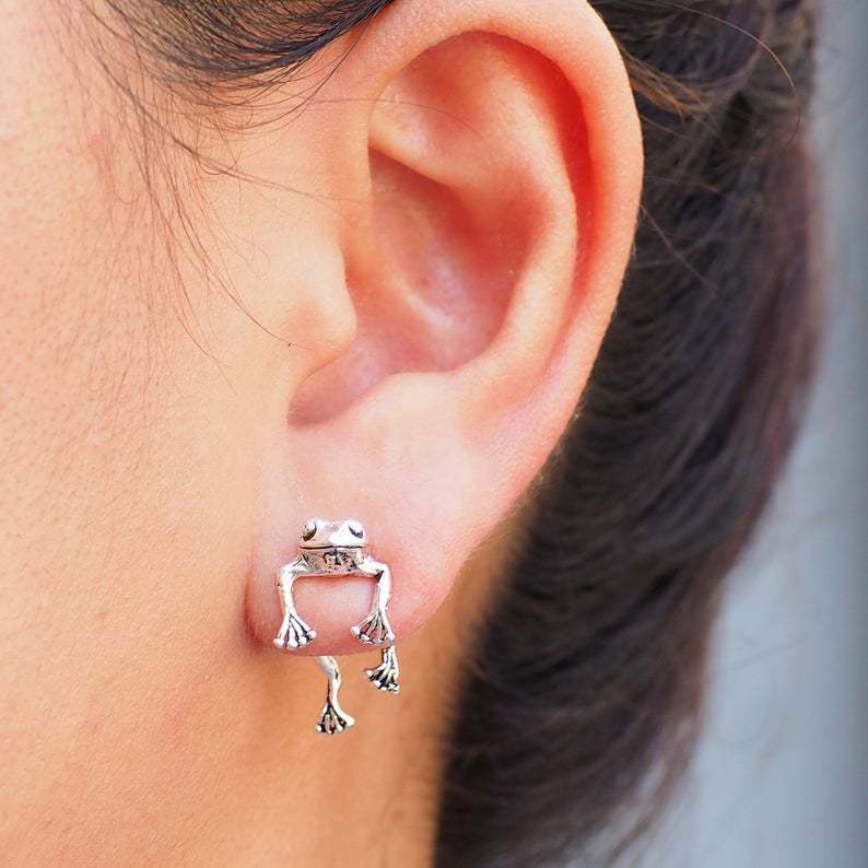 Silver frog-shaped earring worn on a person's ear.