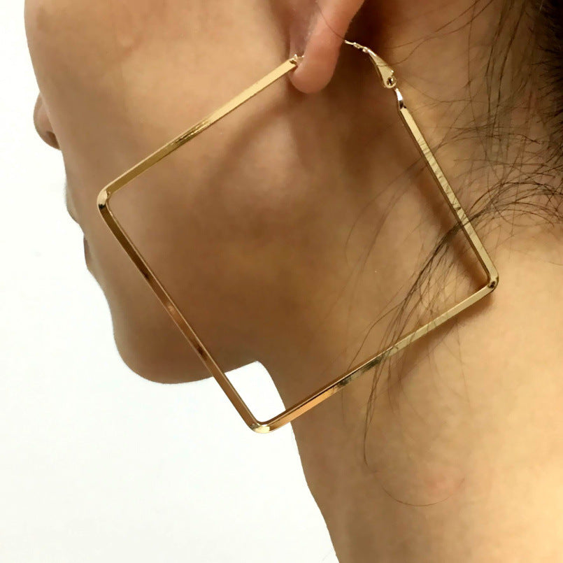 Gold hoop earring being worn on a person's ear against a neutral background