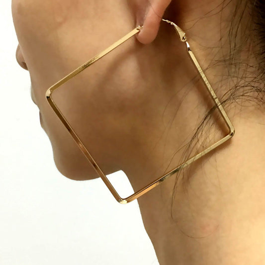 Gold hoop earring being worn on a person's ear against a neutral background