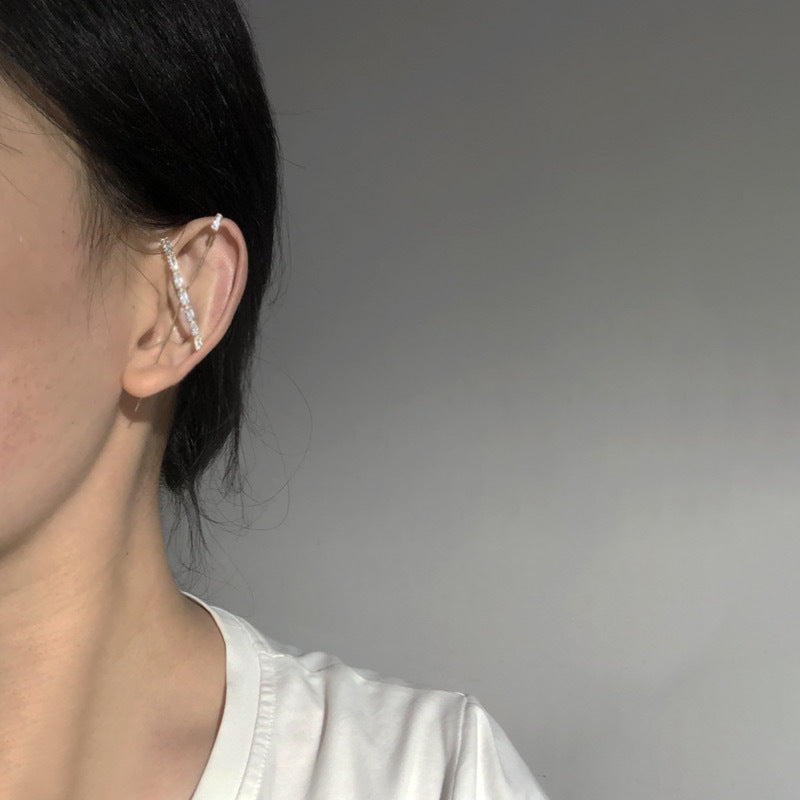 Close-up of a person wearing a diamond earring against a gray background