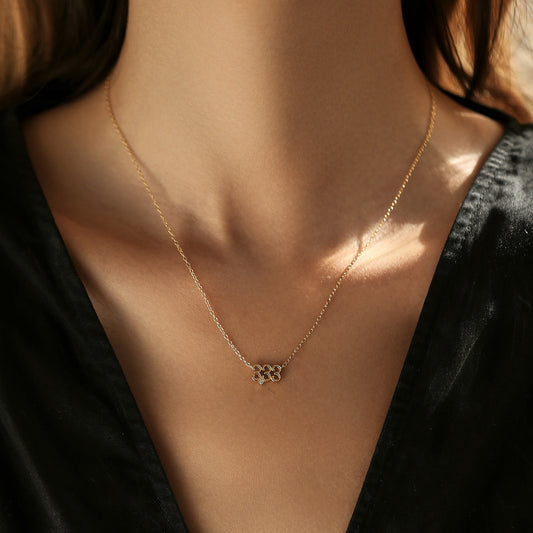 Gold necklace with a clover pendant on a person wearing a black top.