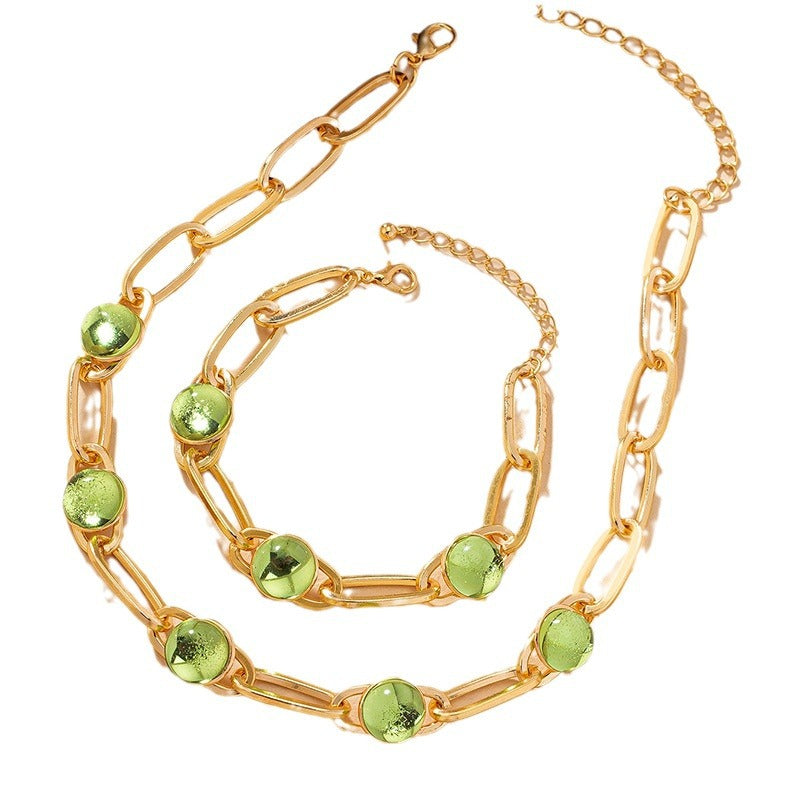Gold chain bracelet with green gemstones on a white background
