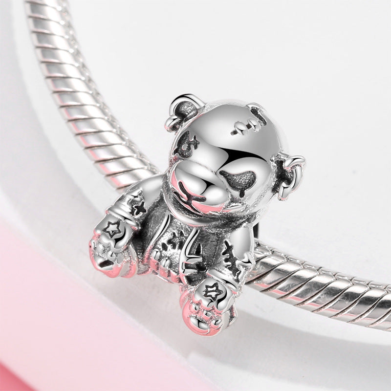 Silver teddy bear charm on a silver bracelet against a light pink background