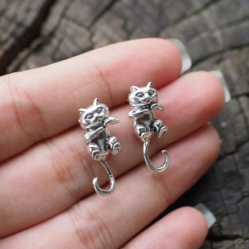 Silver cat-shaped earrings held between fingers against a textured background