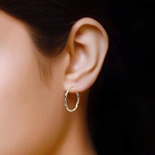 Gold hoop earring worn by a person on a dark background