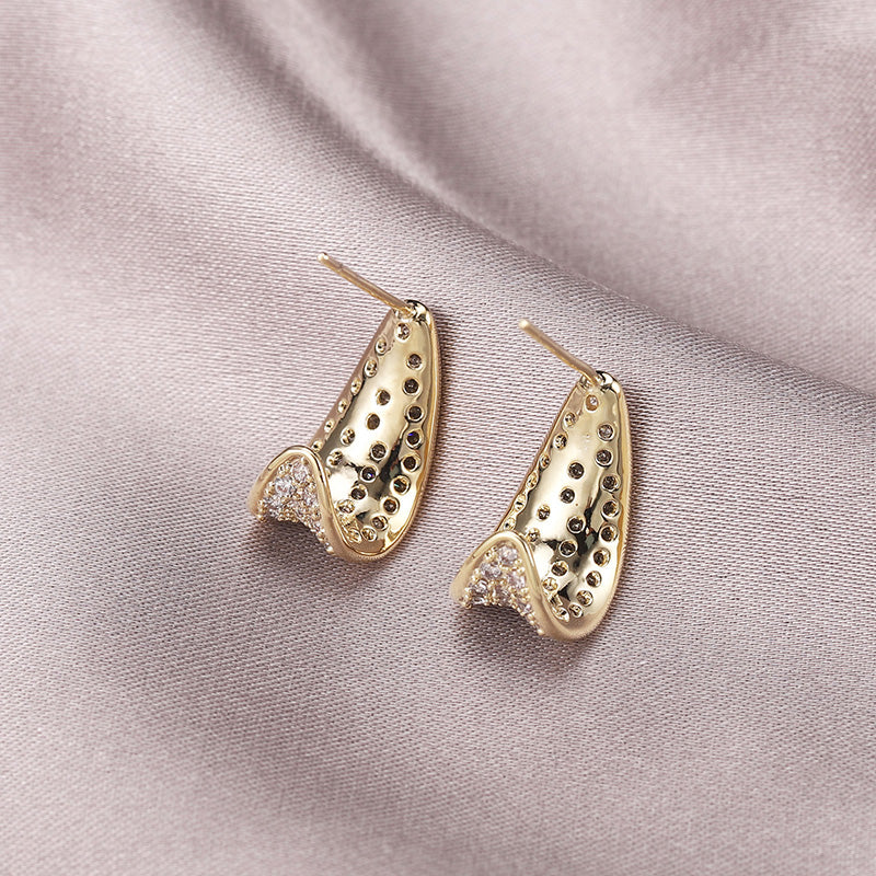 Gold earrings with intricate design on a pink fabric background