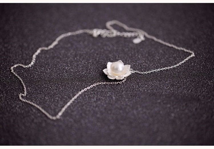 Silver necklace with a flower-shaped pendant on a dark surface