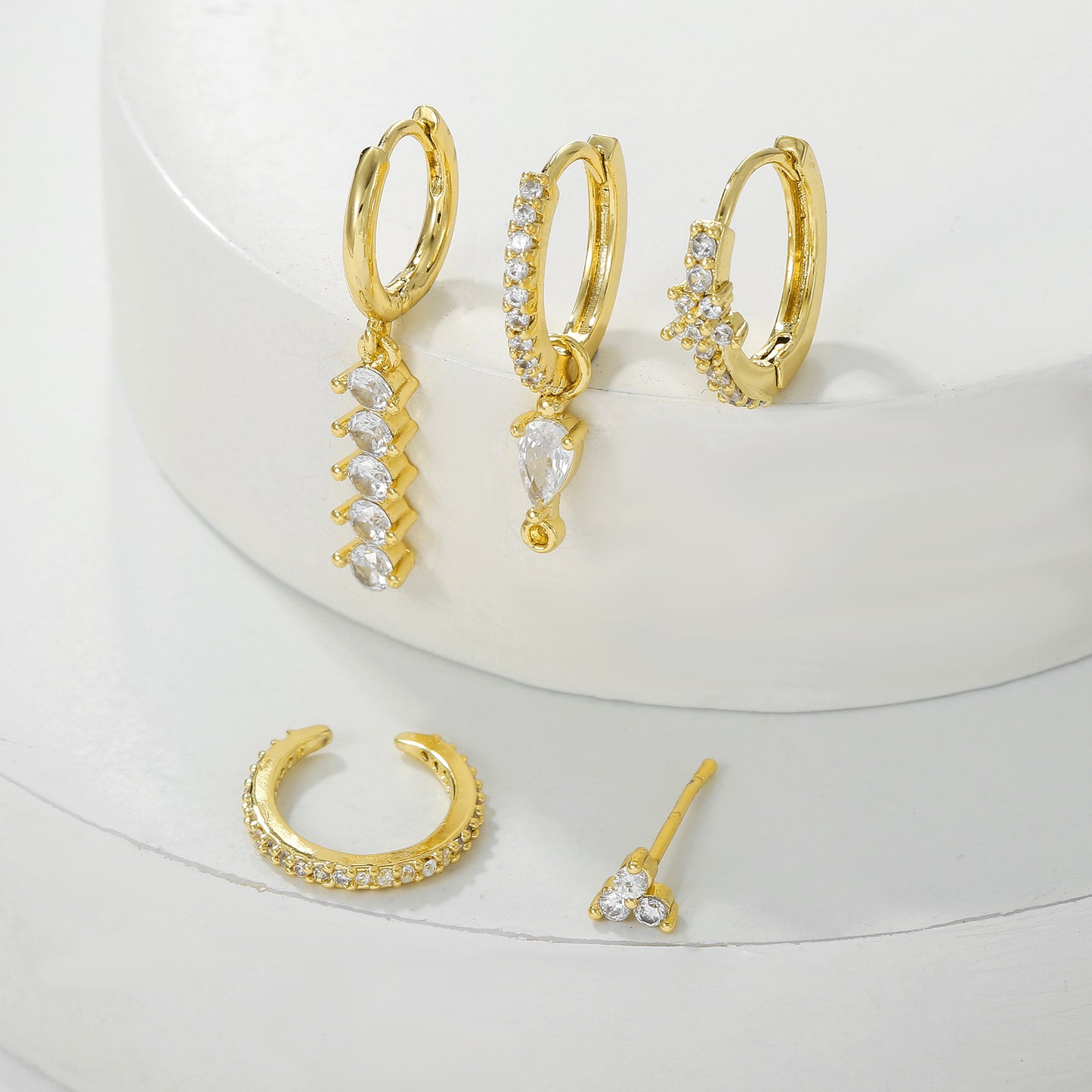 Set of gold hoop earrings with clear gemstones on a white surface