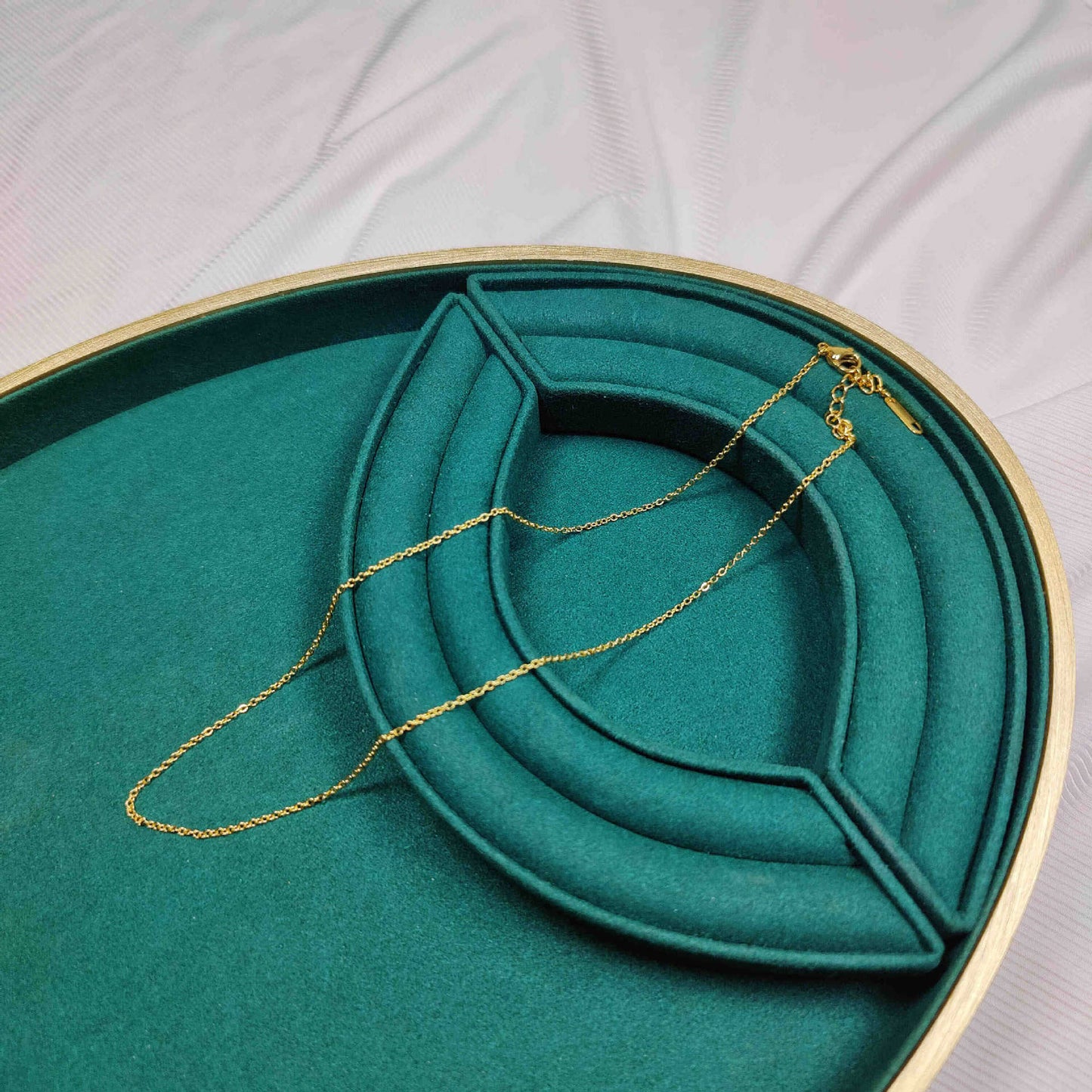 Gold necklace on a green jewelry dish with a gold rim.