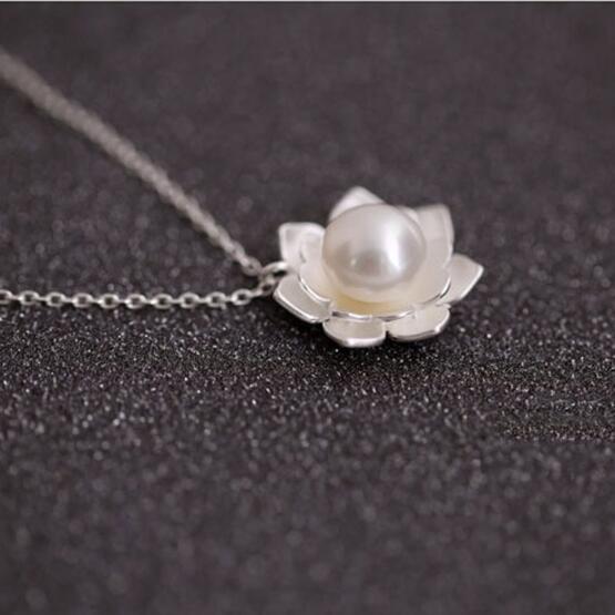 Pearl necklace with silver lotus flower pendant on a dark textured background