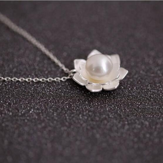 Pearl necklace with silver lotus flower pendant on a dark textured background
