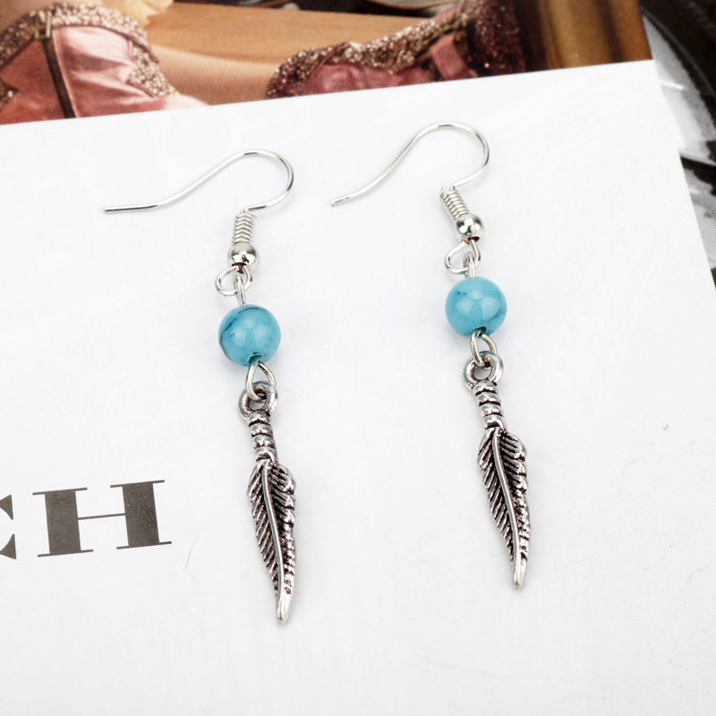 Pair of earrings with blue beads and silver feather charms on a magazine background