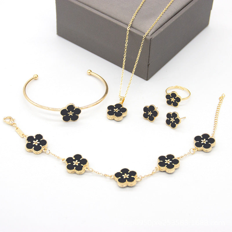 Jewelry set with gold necklaces, bracelet, and earrings with black flower designs on a white background.