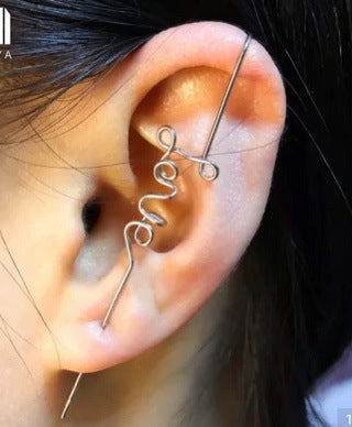 Close-up of an ear with a gold 'love' ear cuff against a dark background