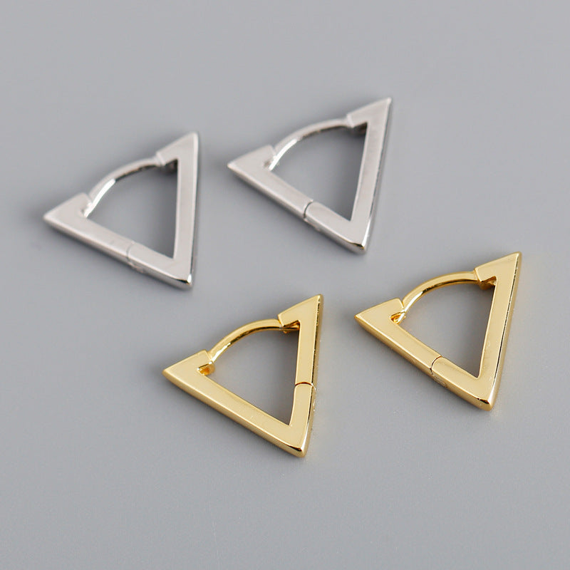 Four triangular gold and silver earrings on a gray background
