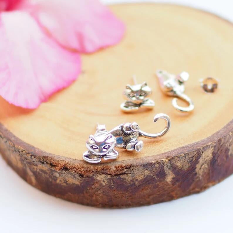 Silver cat-shaped earrings on a wooden surface with pink petals.