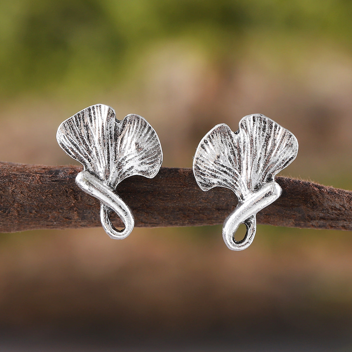 Silver leaf-shaped earrings on a branch with a blurred natural background