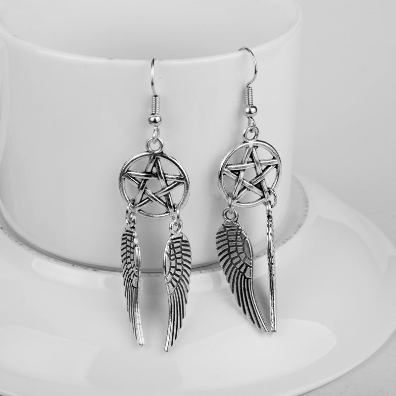 Silver pentagram and wing earrings on a white stand