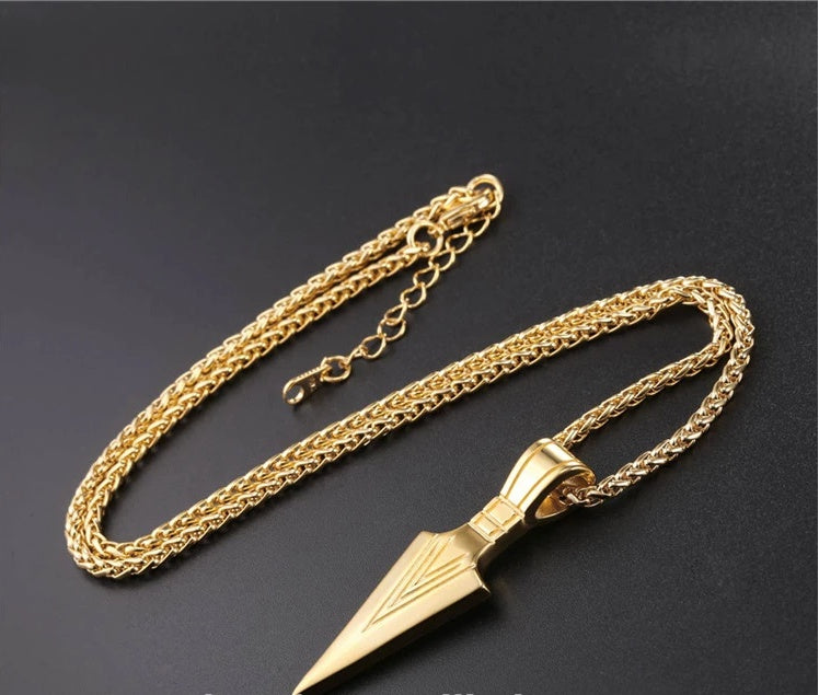 Gold chain necklace with a spearhead pendant on a dark background