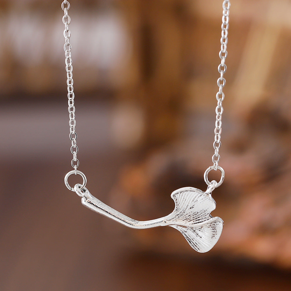 Silver necklace with a leaf-shaped pendant against a blurred natural background