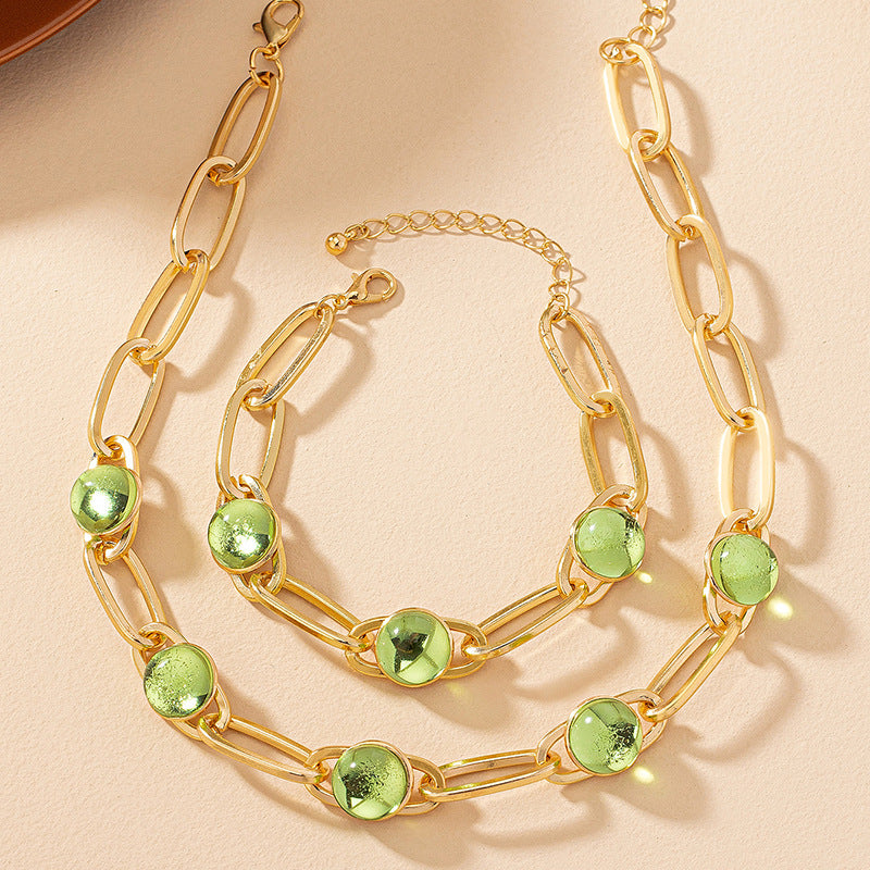Gold chain necklace with green gemstones on a beige background