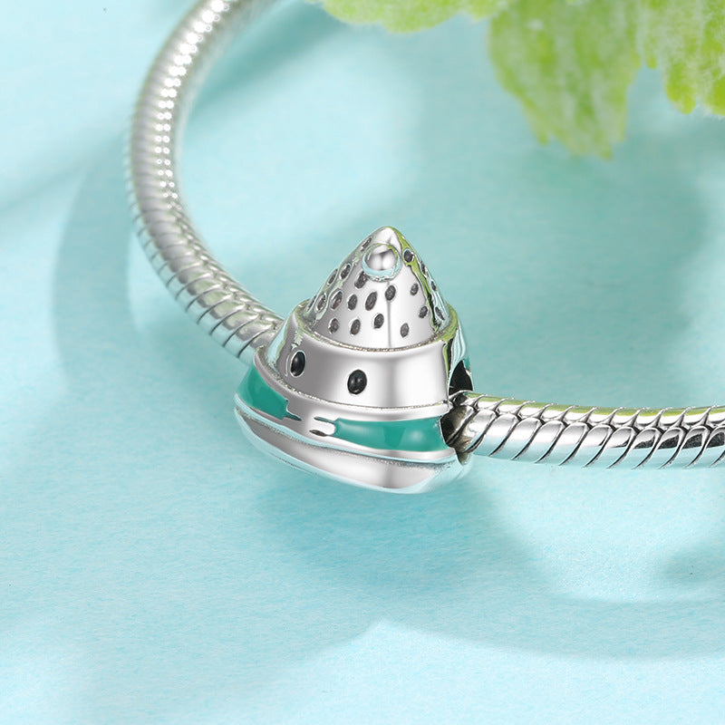 Silver bracelet charm on a light blue background with green leaves