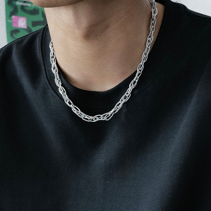 Person wearing a silver chain necklace against a black shirt.