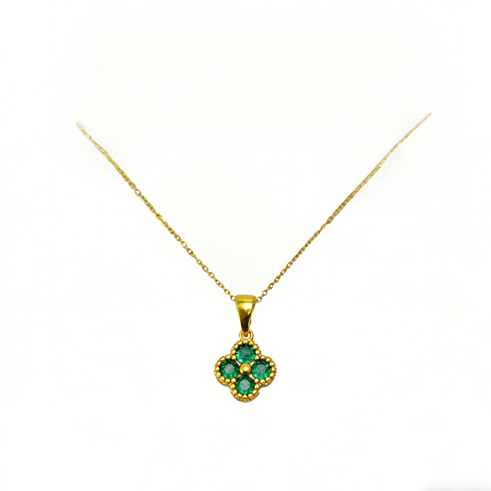 Gold necklace with a clover-shaped pendant featuring green gemstones on a white background
