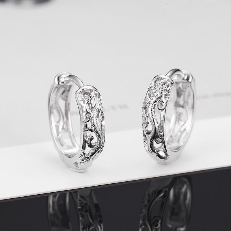 Pair of silver hoop earrings with intricate designs on a reflective surface.