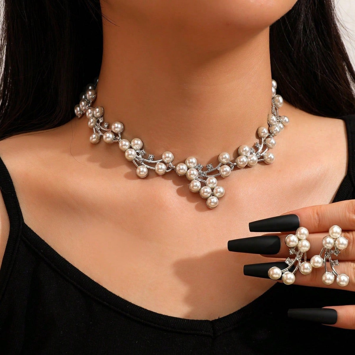 Pearl necklace worn by a person with black nail polish on a neutral background