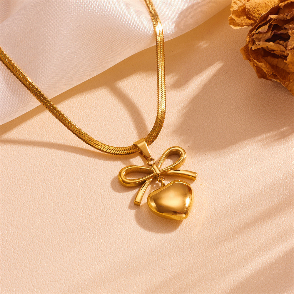 Gold necklace with a heart and bow pendant on a beige background