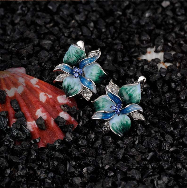 Pair of floral earrings with green and blue design on a black textured surface.