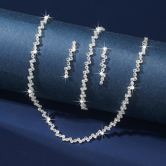Silver necklace and earrings set on a blue fabric background