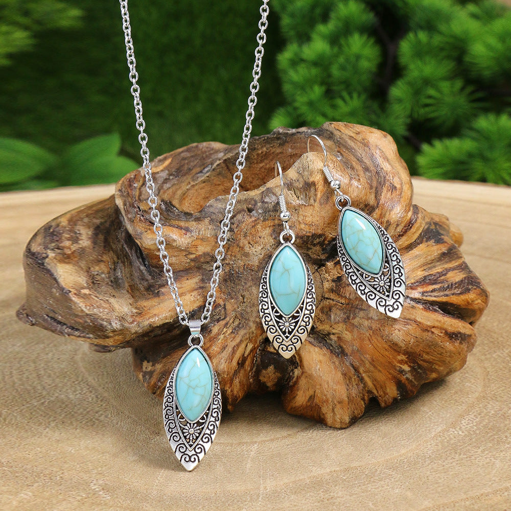 Turquoise jewelry set with necklace and earrings on a wooden surface with greenery in the background