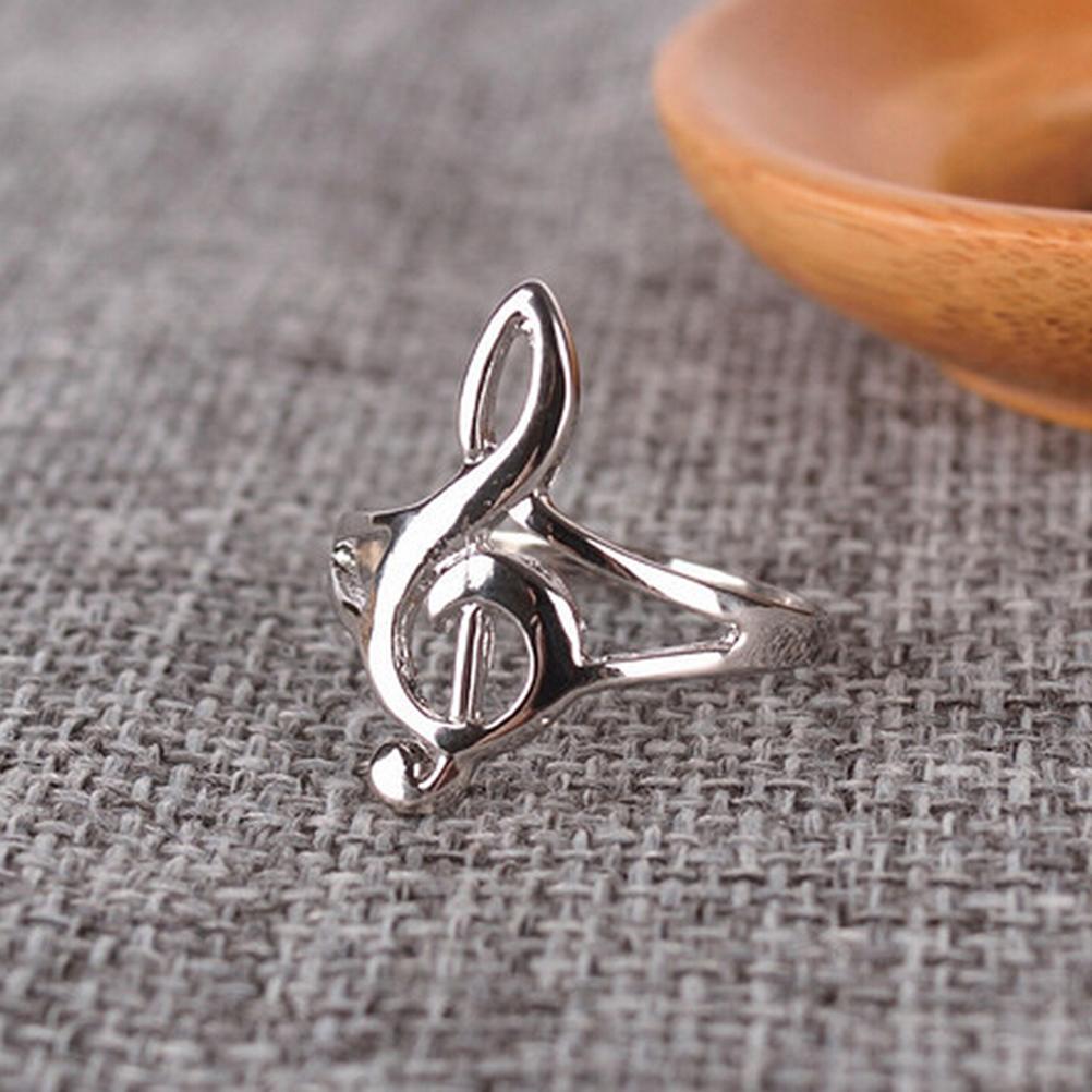 Silver treble clef ring on a textured gray surface with a wooden object in the background