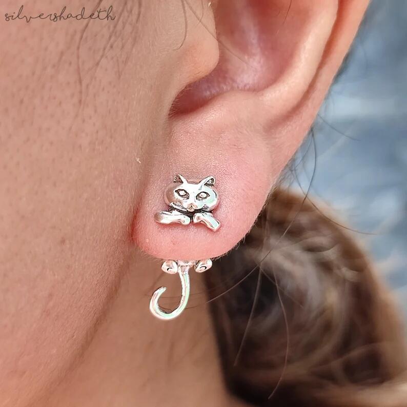 Silver cat-shaped earring worn on a person's ear with a blurred background