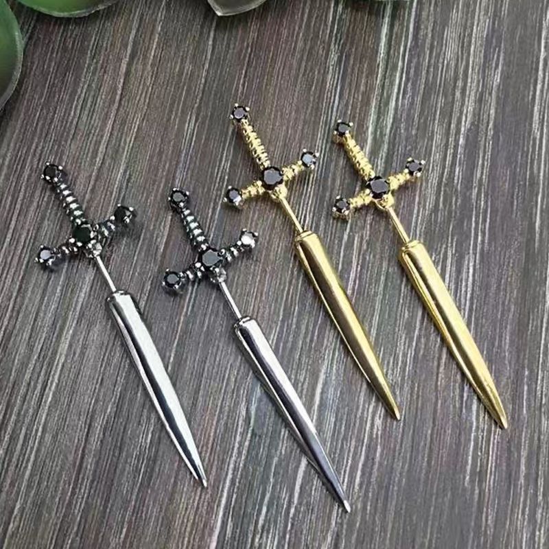 Four decorative sword-shaped pins in silver, gold, and black on a wooden surface.