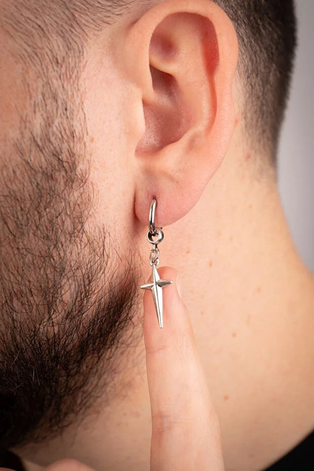 Silver cross earring worn by a person with a neutral background