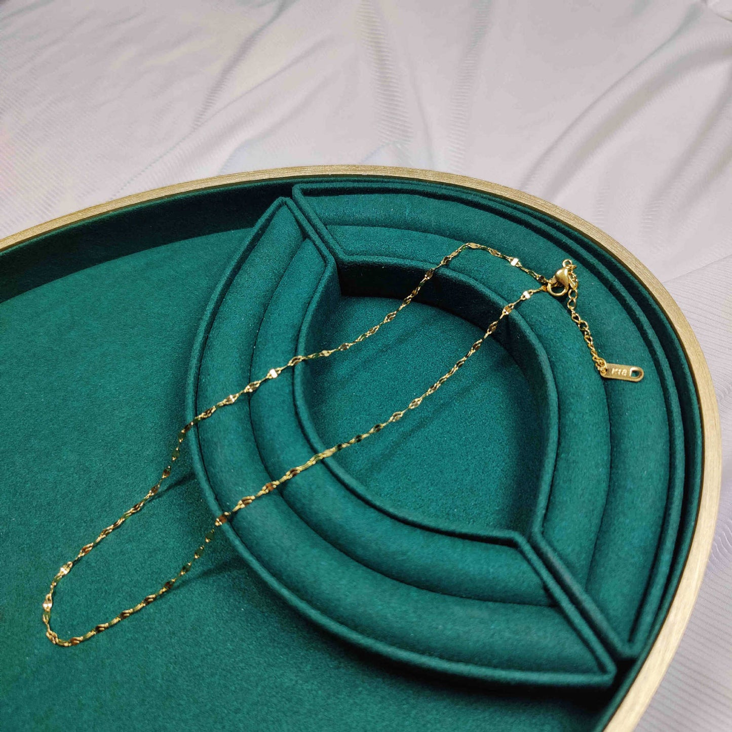 Gold necklace on a green jewelry box with a white background