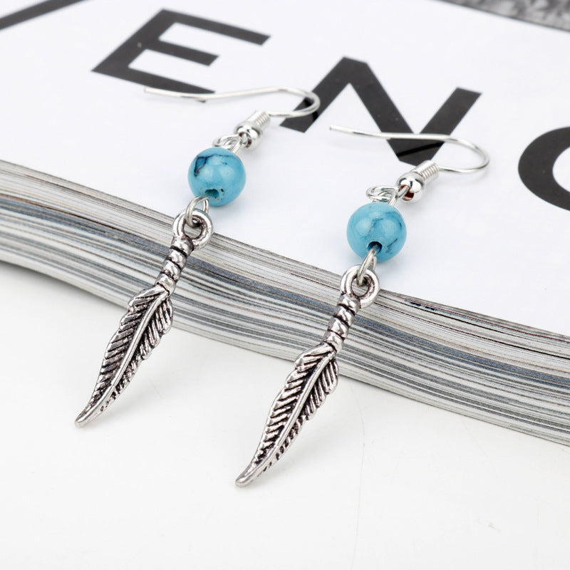 Silver feather earrings with blue beads on a magazine page