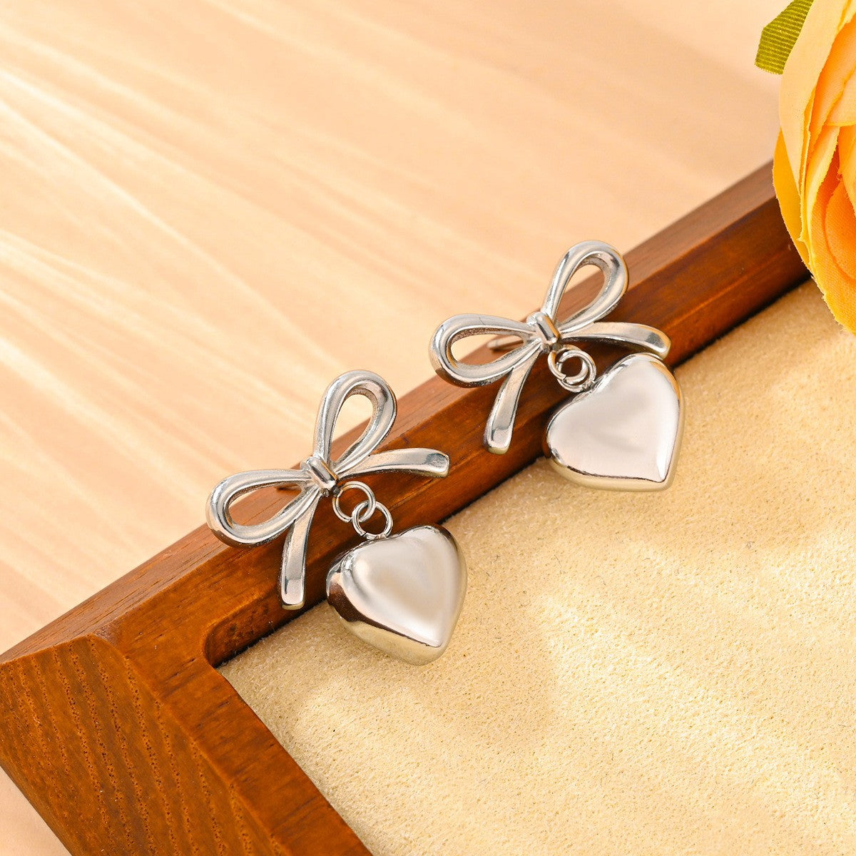 Silver bow and heart earrings on a wooden surface with a floral background